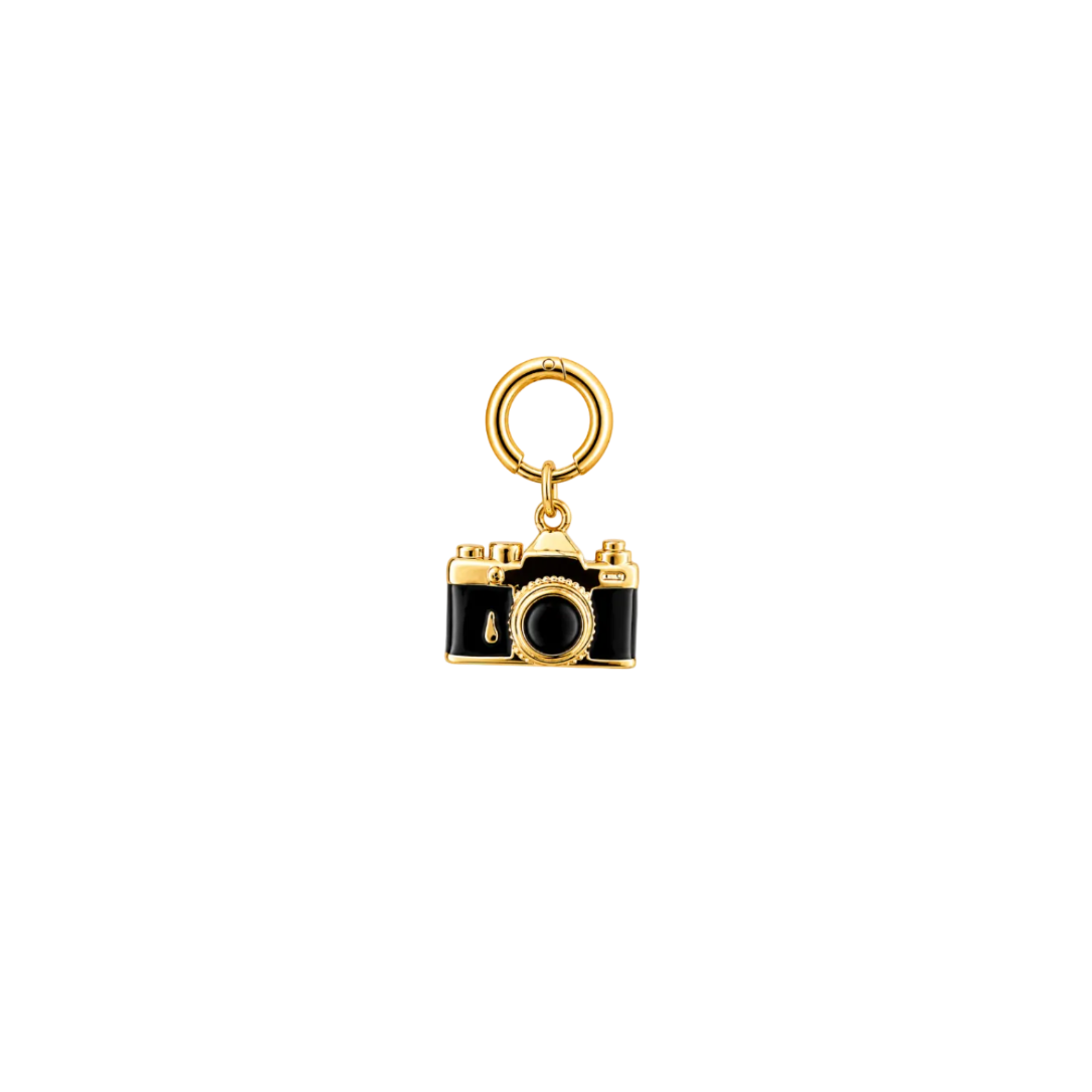 A small camera-shaped charm with a gold-tone metal body and black enamel details, attached to a gold-tone ring, shown on a plain white background.