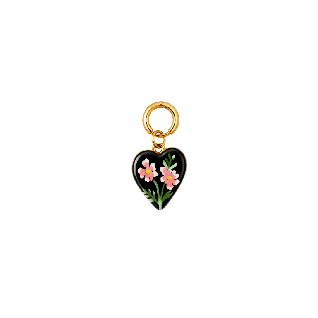 A heart-shaped black enamel charm with pink and white flowers and green leaves, attached to a gold-tone split ring, shown on a plain white background.