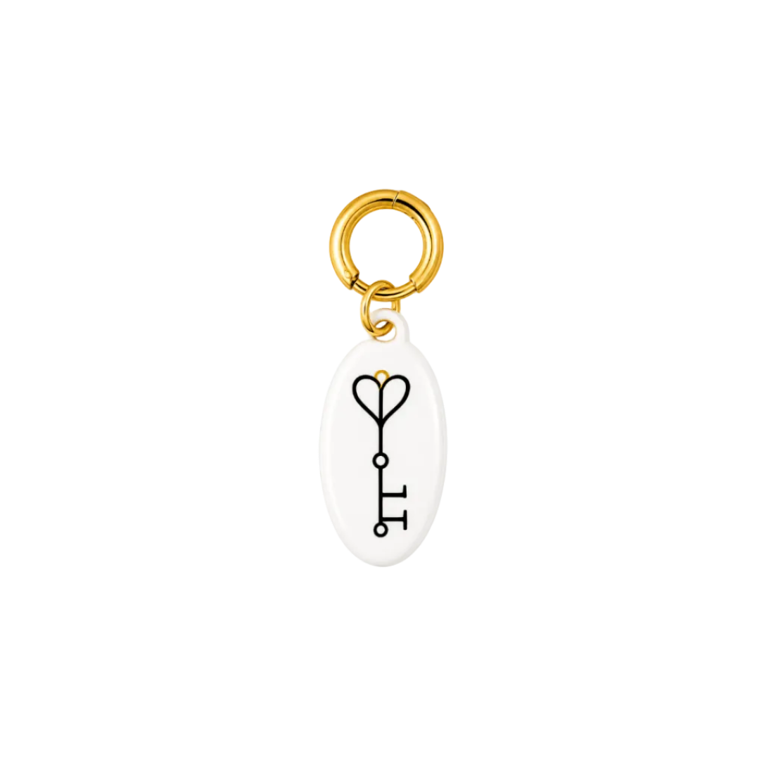 A white oval key-shaped charm with a black outline key graphic and a small gold heart at the top, attached to a shiny gold split ring on a plain white background.